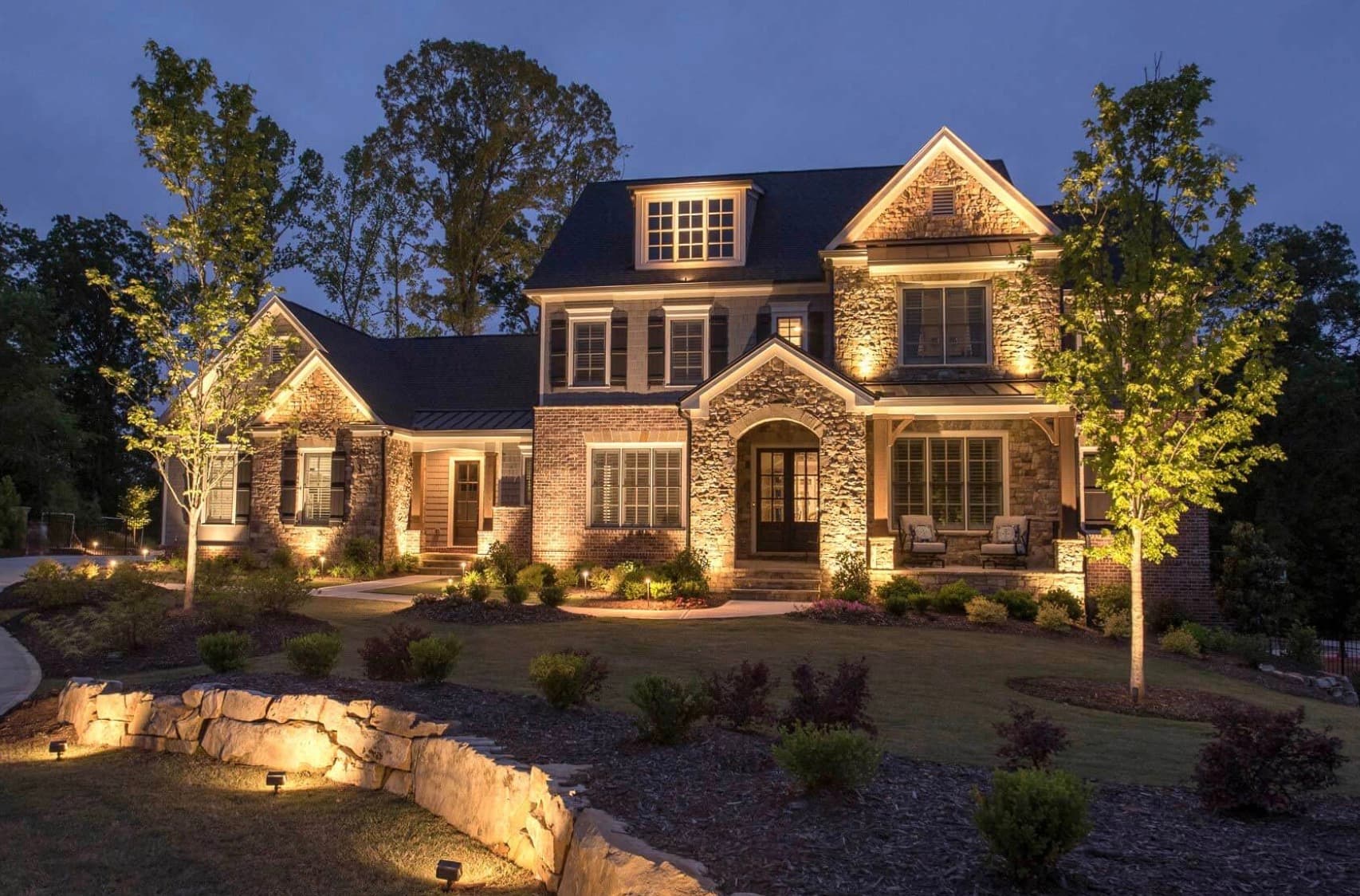 Warm landscape lighting around a stone estate at dusk